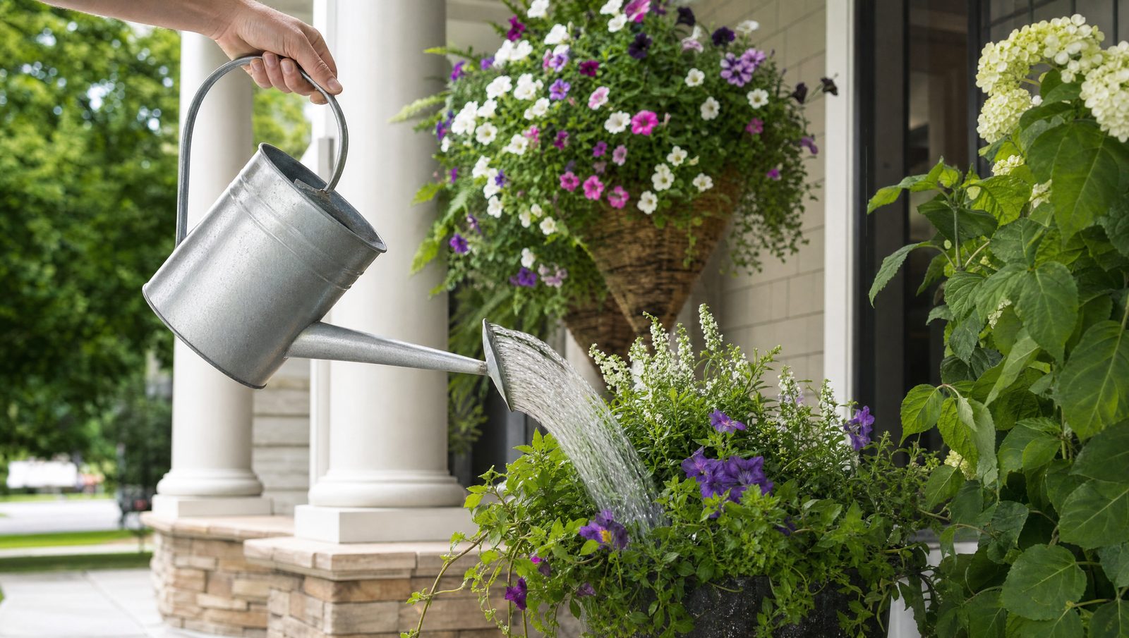 A watering can tending hanging baskets and pots on a front porch